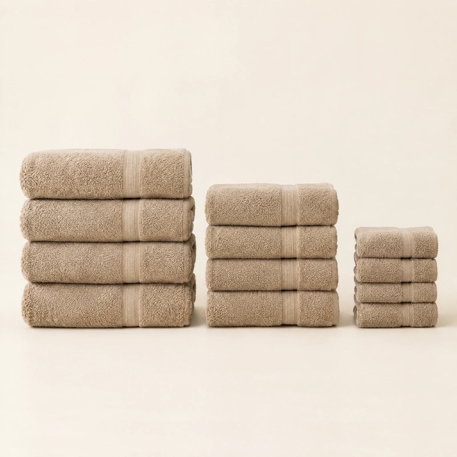Twelve sand colored towels folded in stacks of bath towels, hand towels and washcloths on a cream backdrop
