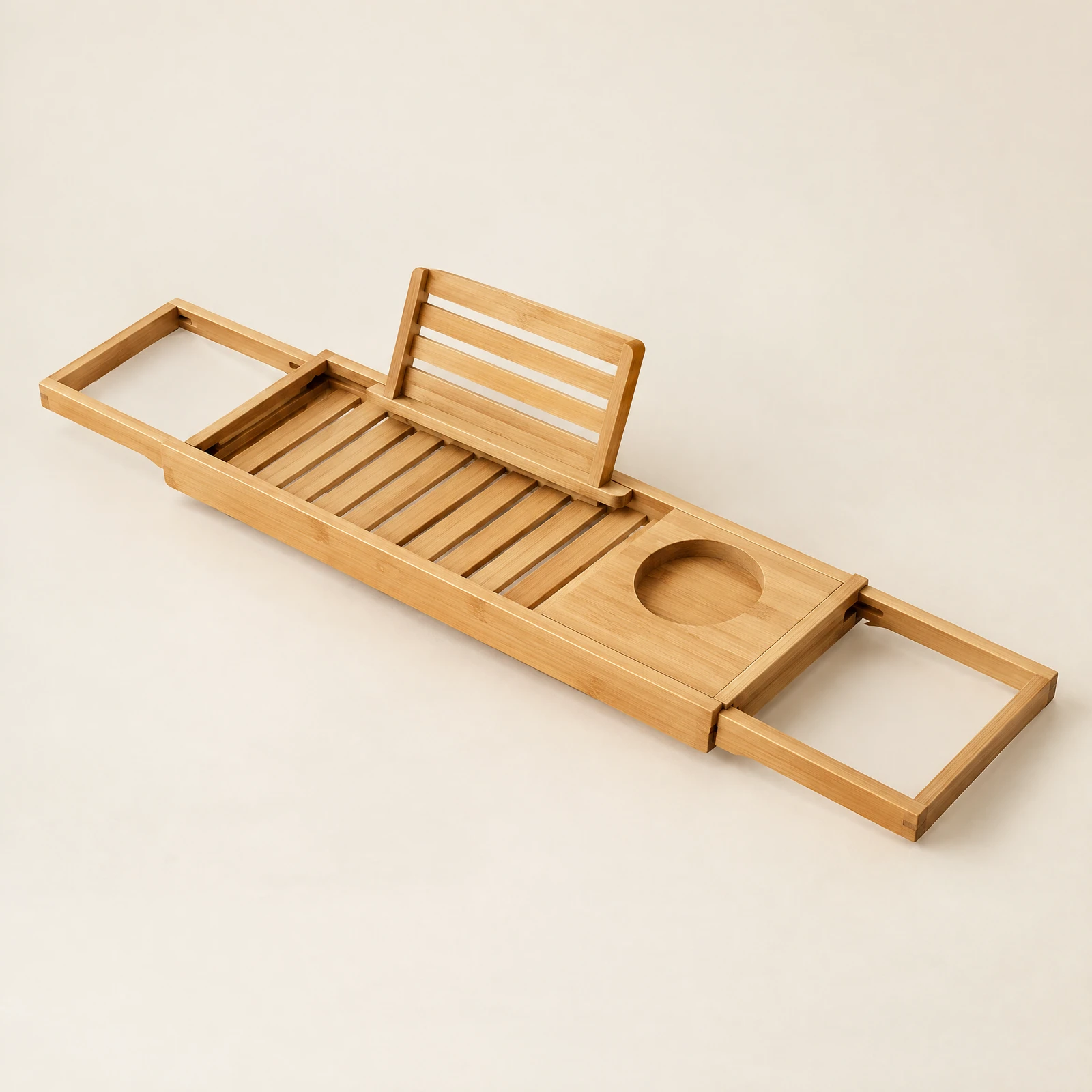 Expandable slatted bathtub tray with extending side arms, a book rest and a round cup cutout shown on a cream backdrop