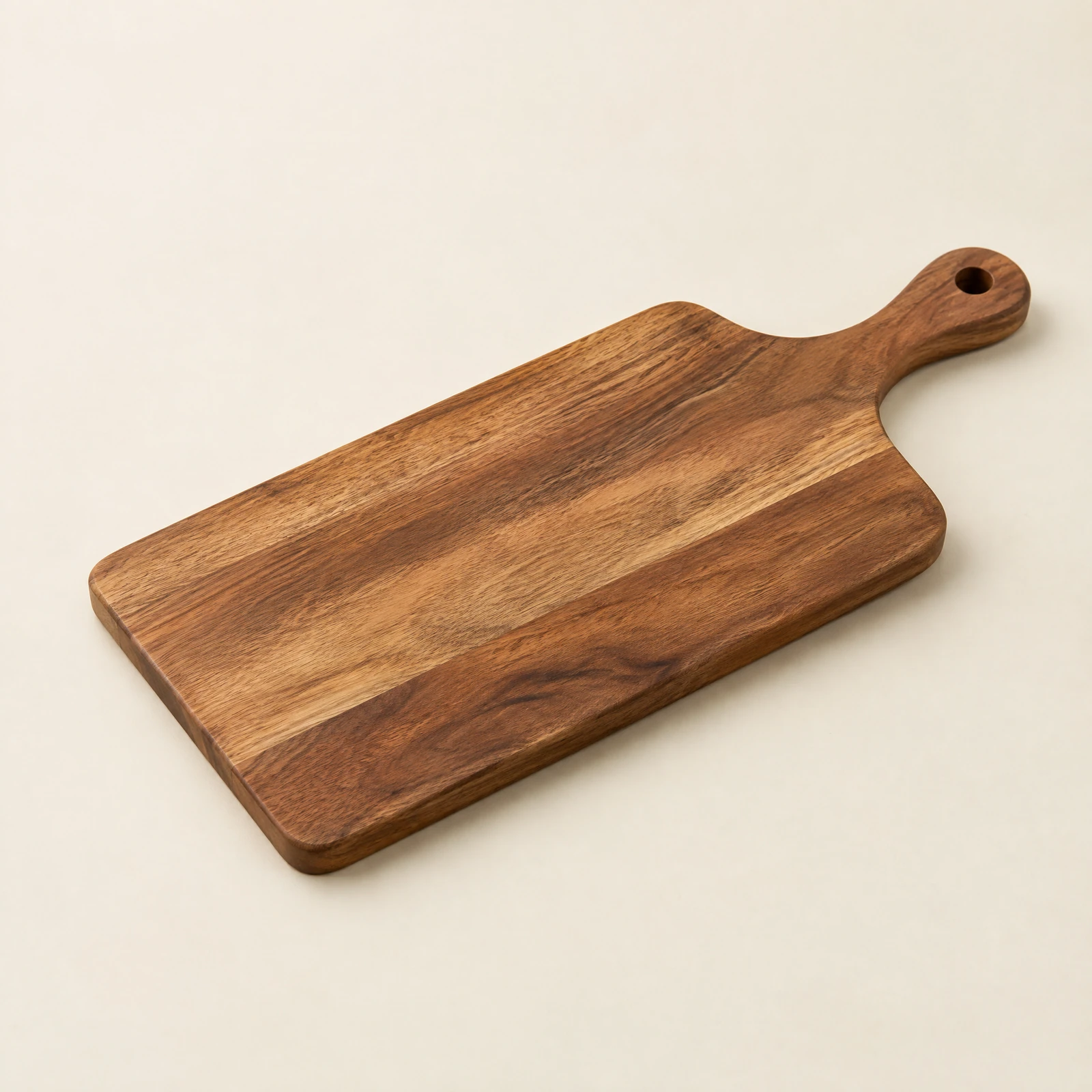 Rectangular natural wood-tone serving board with a rounded handle and hanging hole on a cream backdrop
