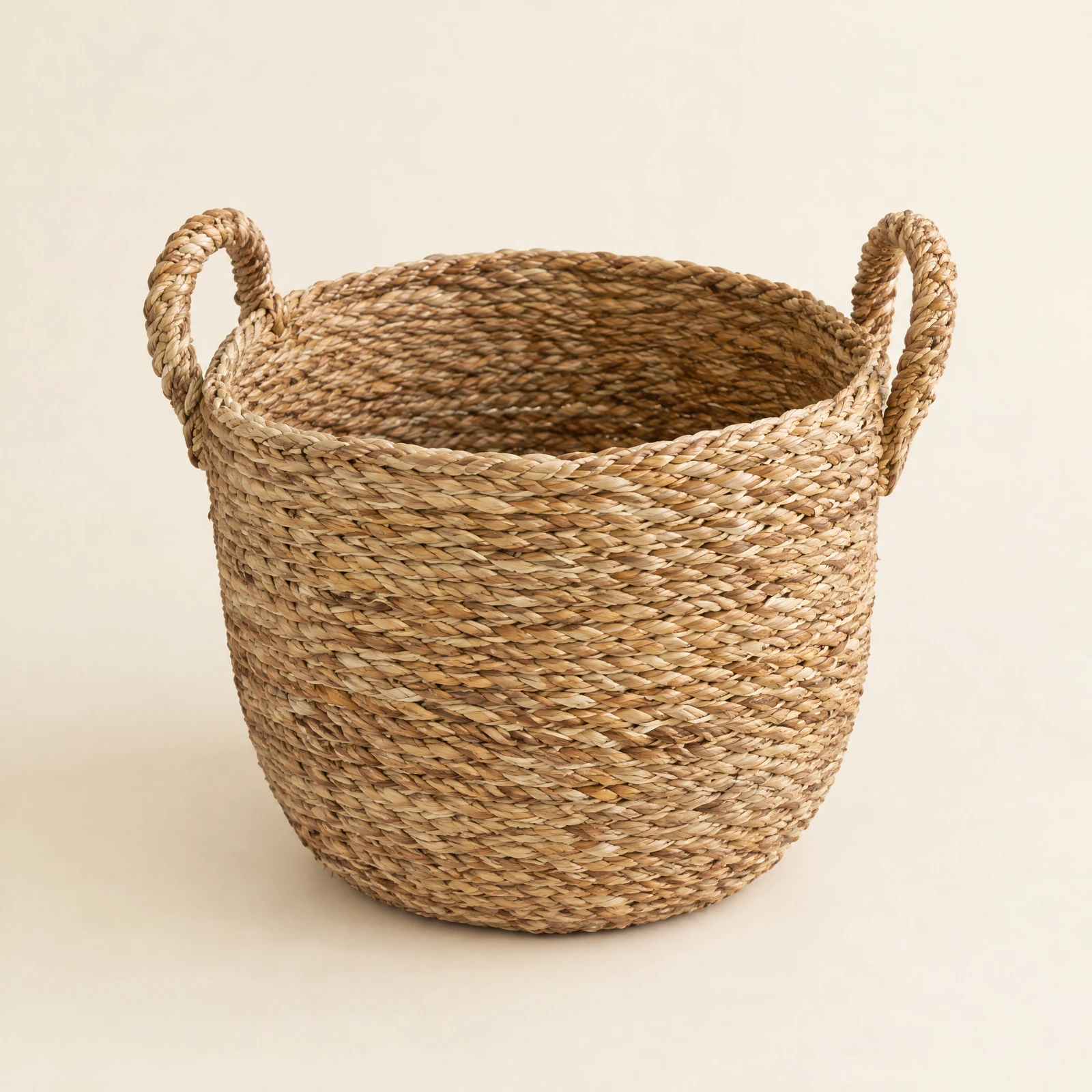 Round woven storage basket with two looped handles on a cream backdrop